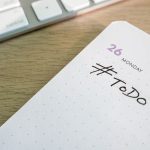 Close-up of a to-do list next to a computer keyboard on a desk.